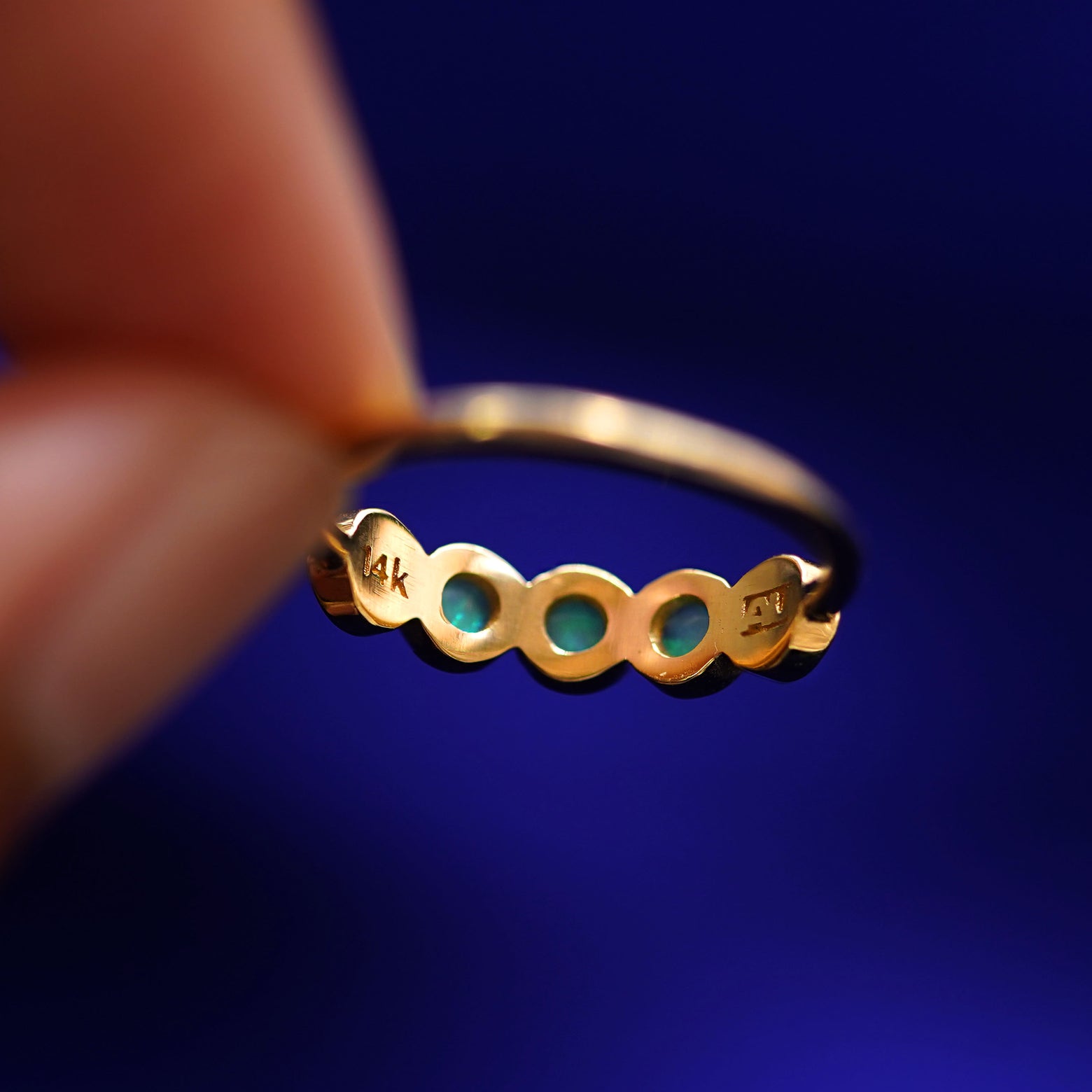 A hand holding a 5 Gemstones Ring with opals to show the underside view