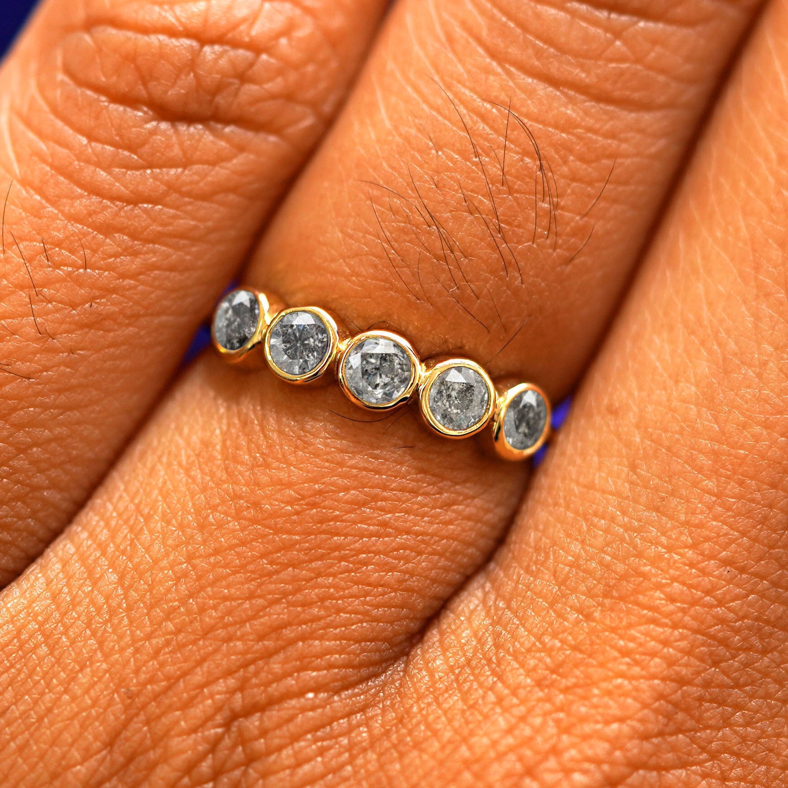 Close up view of a model's fingers wearing a 14k yellow gold Five Diamond Ring with salt and pepper diamonds