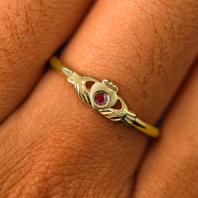Close up view of a model's fingers wearing a 14k yellow gold garnet Thin Gemstone Claddagh Ring