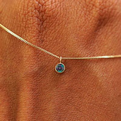 Close up view of a 14k yellow gold Alexandrite Necklace draped across the back of a model's hand