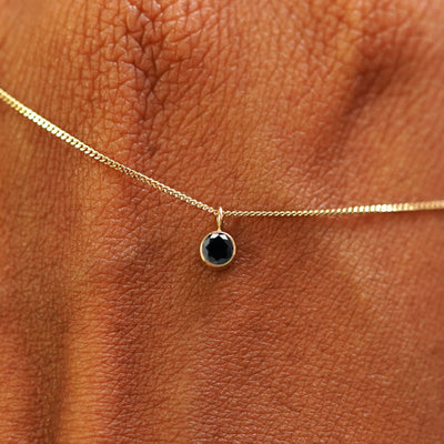 Close up view of a 14k yellow gold Black Diamond Necklace draped across the back of a model's hand
