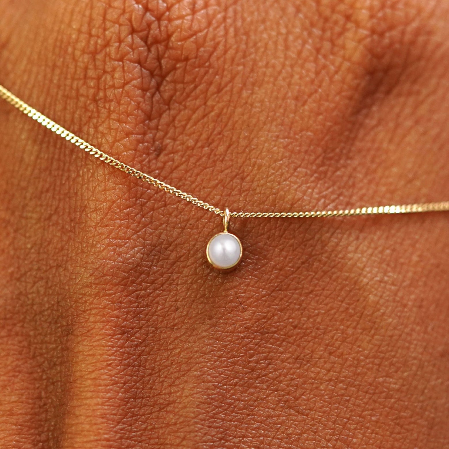 Close up view of a 14k yellow gold Pearl Necklace draped across the back of a model's hand