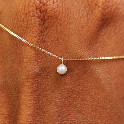 Close up view of a 14k yellow gold Pearl Necklace draped across the back of a model's hand