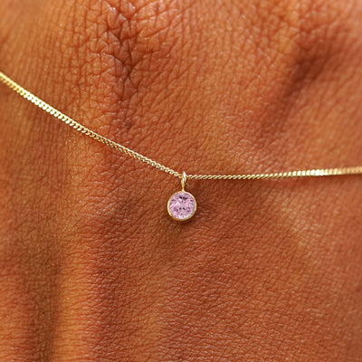 Close up view of a 14k yellow gold Pink Sapphire Necklace draped across the back of a model's hand