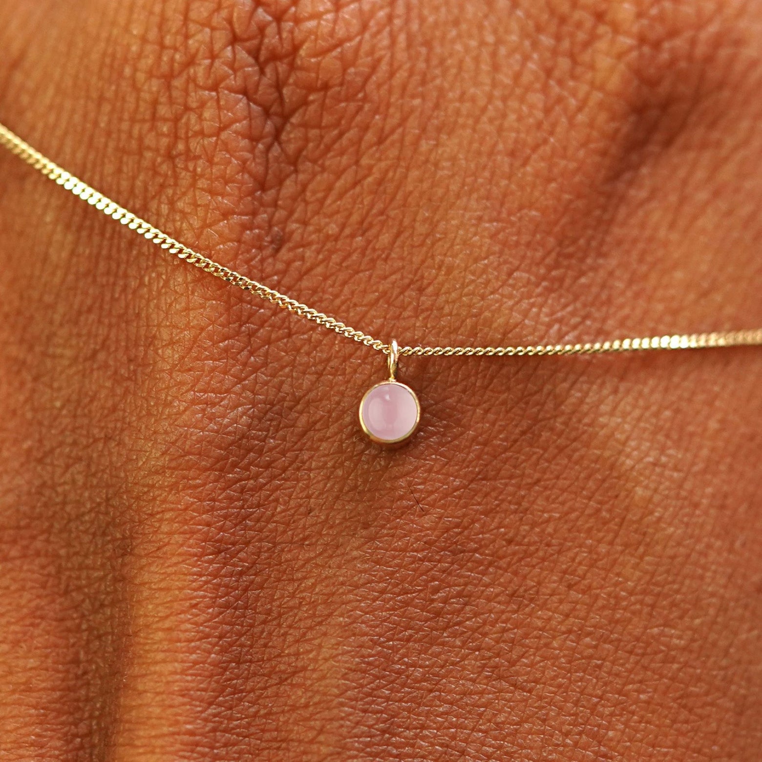 Close up view of a 14k yellow gold Rose Quartz Necklace draped across the back of a model's hand
