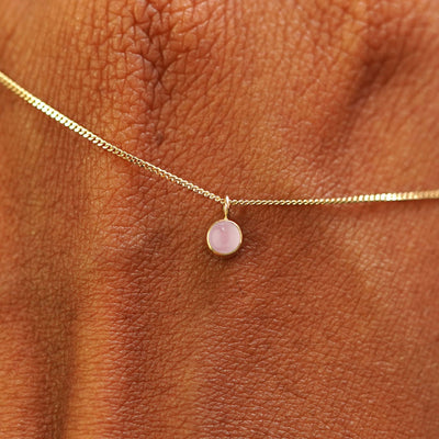 Close up view of a 14k yellow gold Rose Quartz Necklace draped across the back of a model's hand
