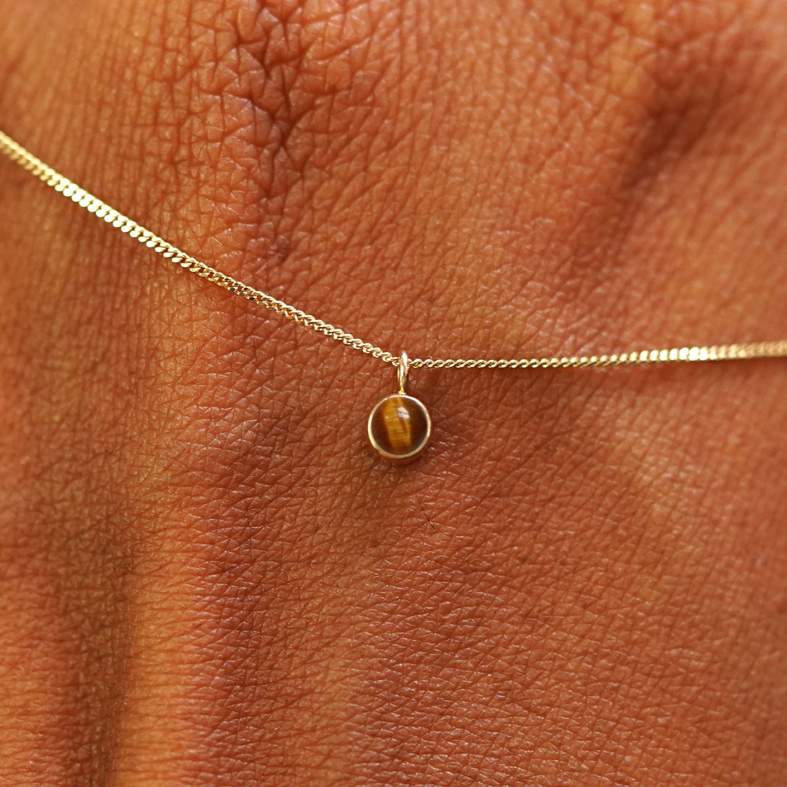 Close up view of a 14k yellow gold Tiger Eye Necklace draped across the back of a model's hand