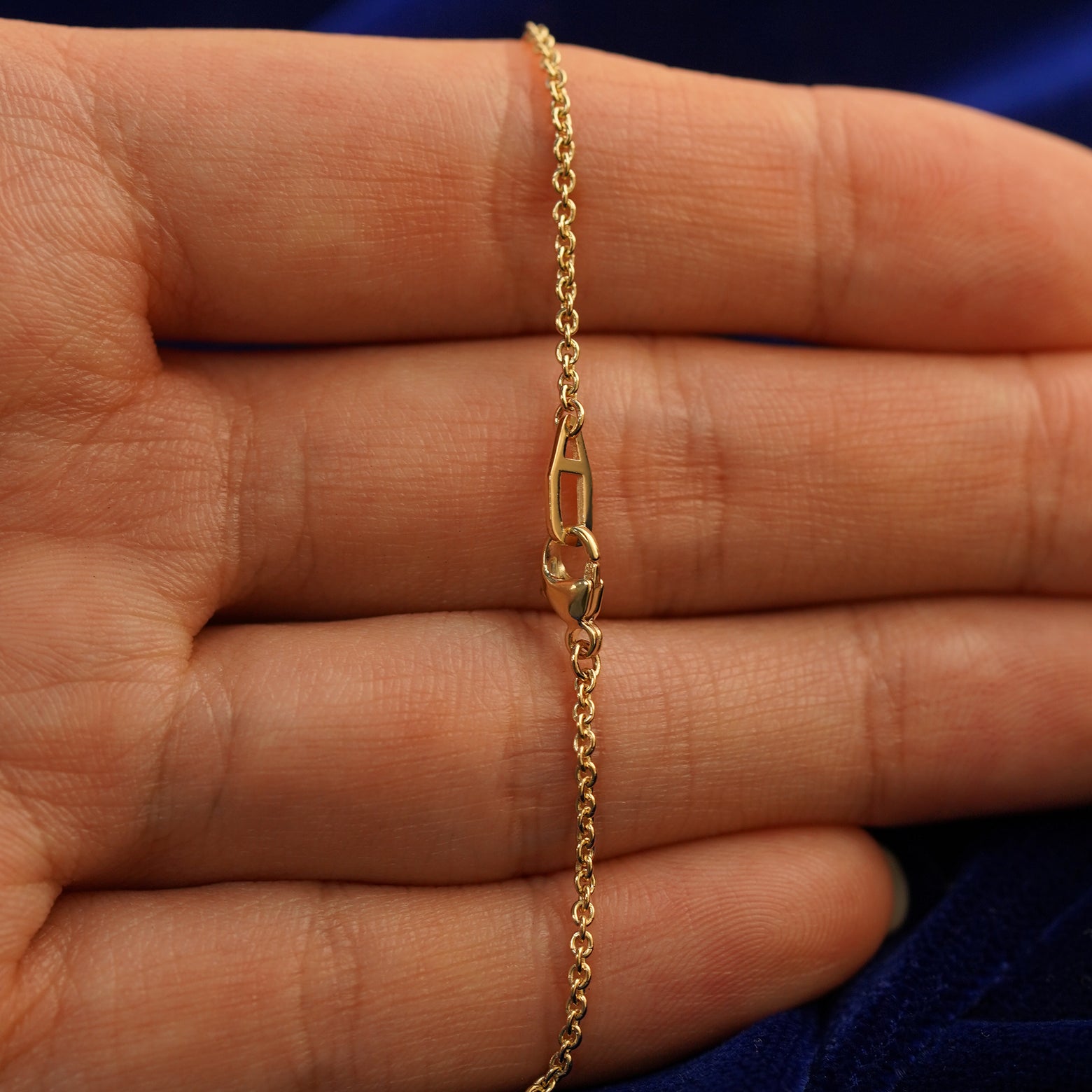 A model's hand holding an Automic Gold AU lobster claw lock on a yellow gold Thick Cable Chain