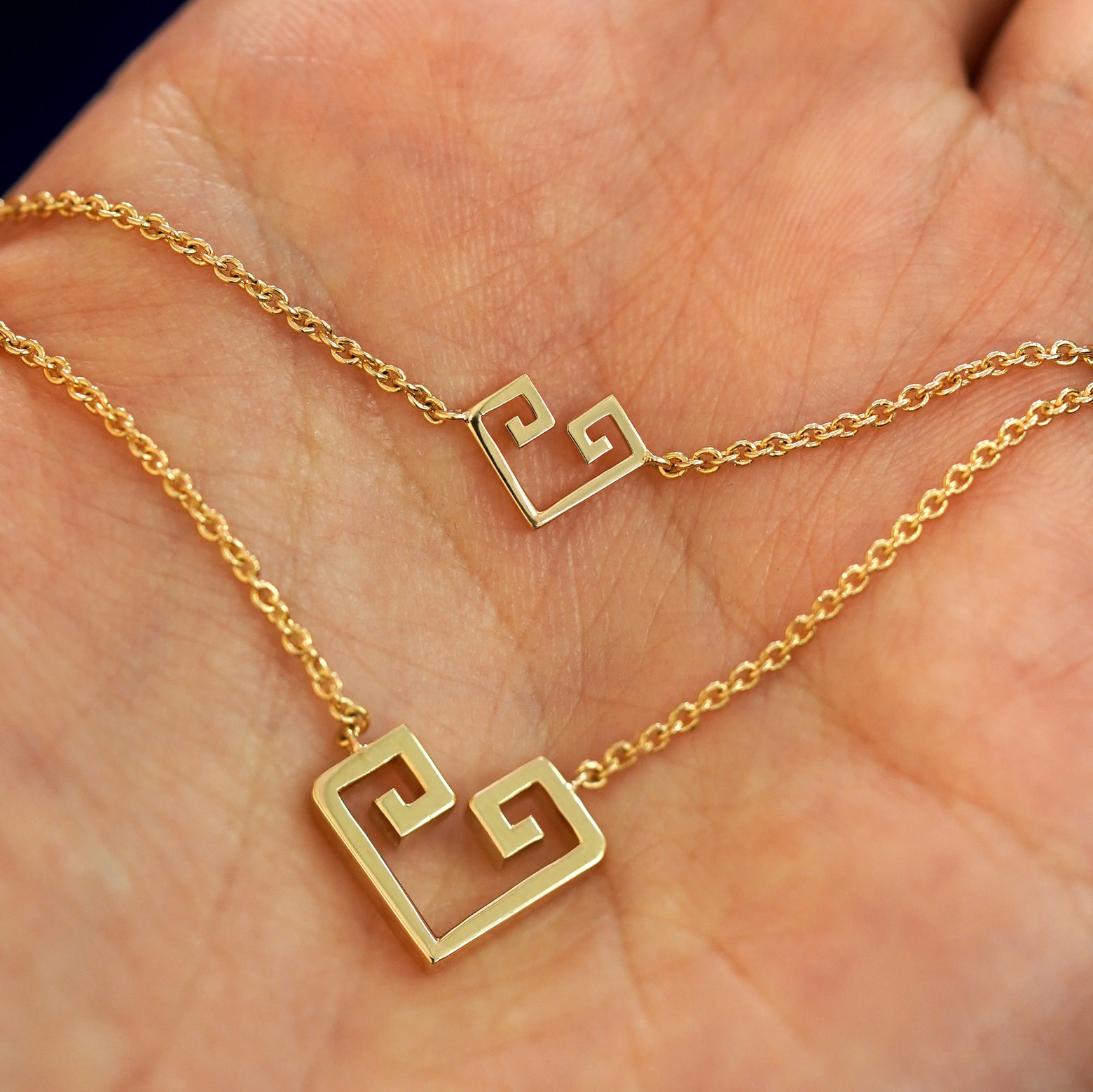 A geometric Chere heart bracelet and large necklace layered on a model's palm
