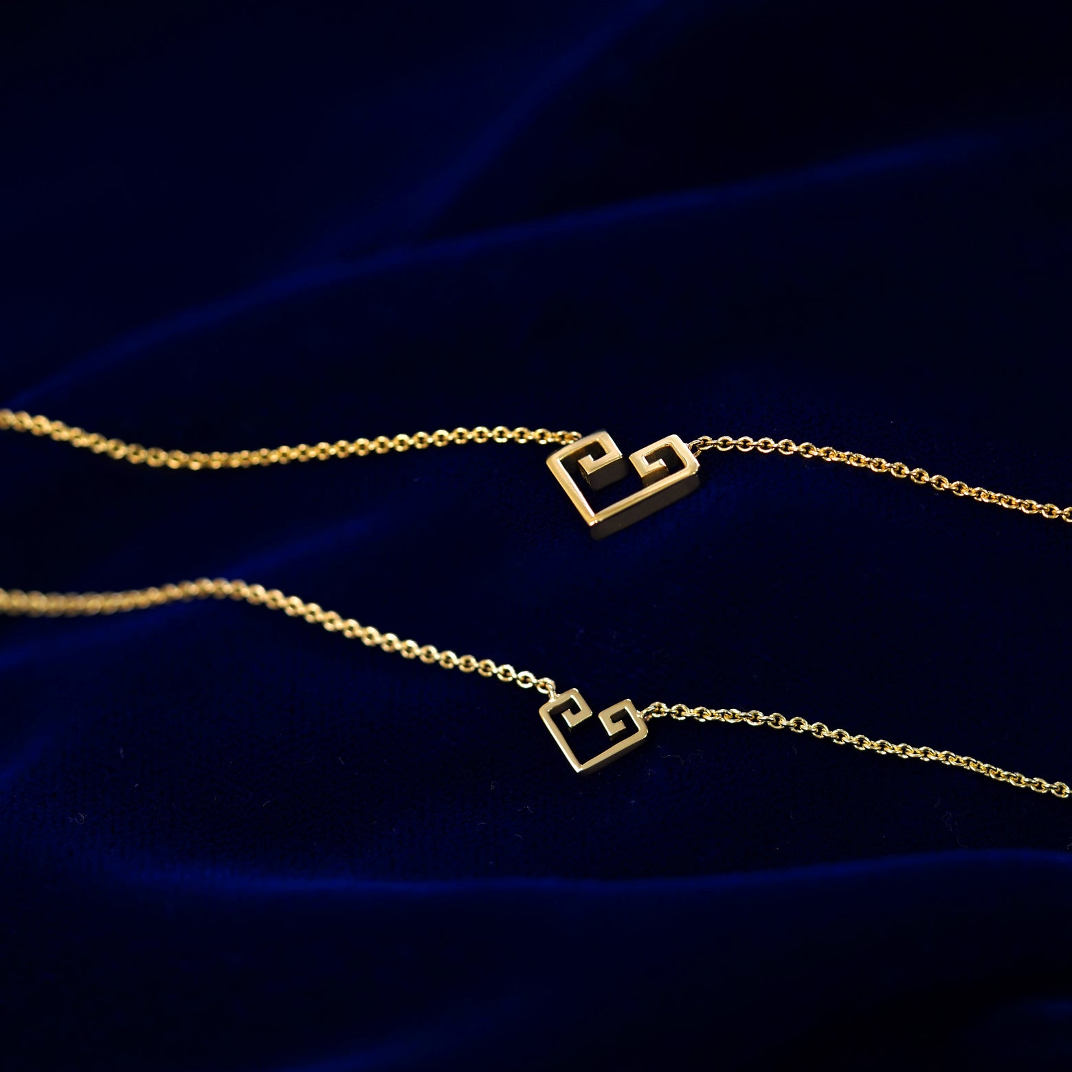 Small and large geometric heart pendant necklaces layered on a dark blue cloth