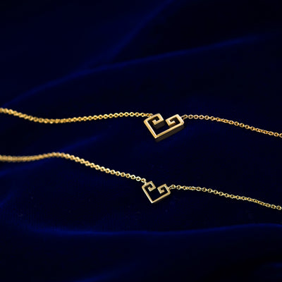 Small and large geometric heart pendant necklaces layered on a dark blue cloth