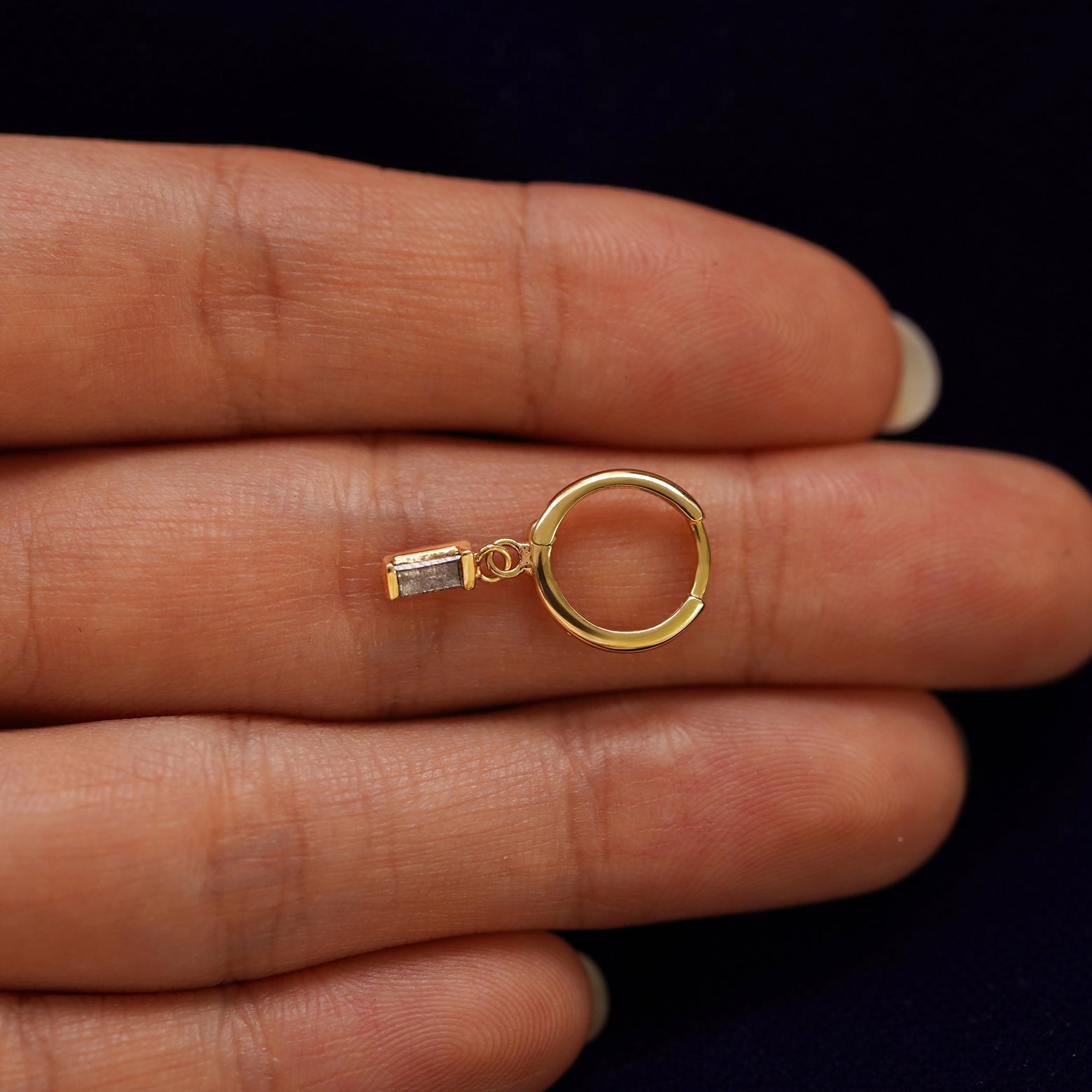 A solid 14k yellow gold Baguette Diamond Dangle Huggie Hoop closed on a model's fingertips