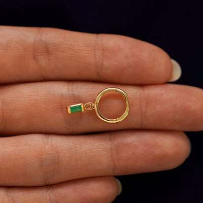A solid 14k yellow gold Baguette Emerald Dangle Huggie Hoop closed on a model's fingertips