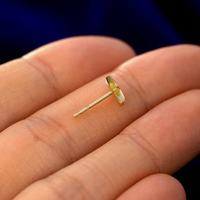 A 14k gold Starburst Earring in a model's hand resting on its side to show the thickness of the earring 