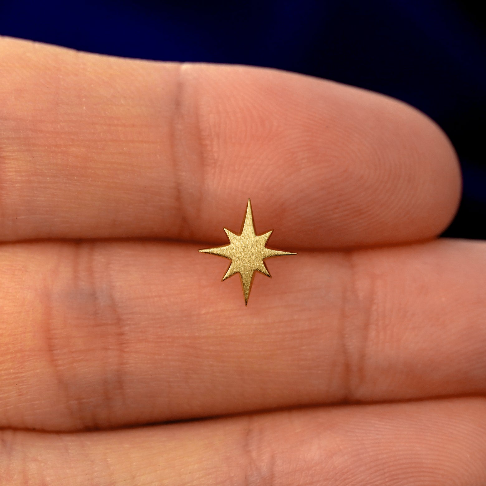 A model holding a solid gold Starburst stud earring between two fingers