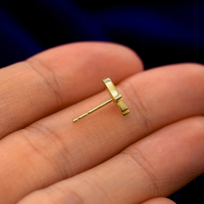A 14k gold Hamsa Earring in a model's hand resting on its side to show the thickness of the earring