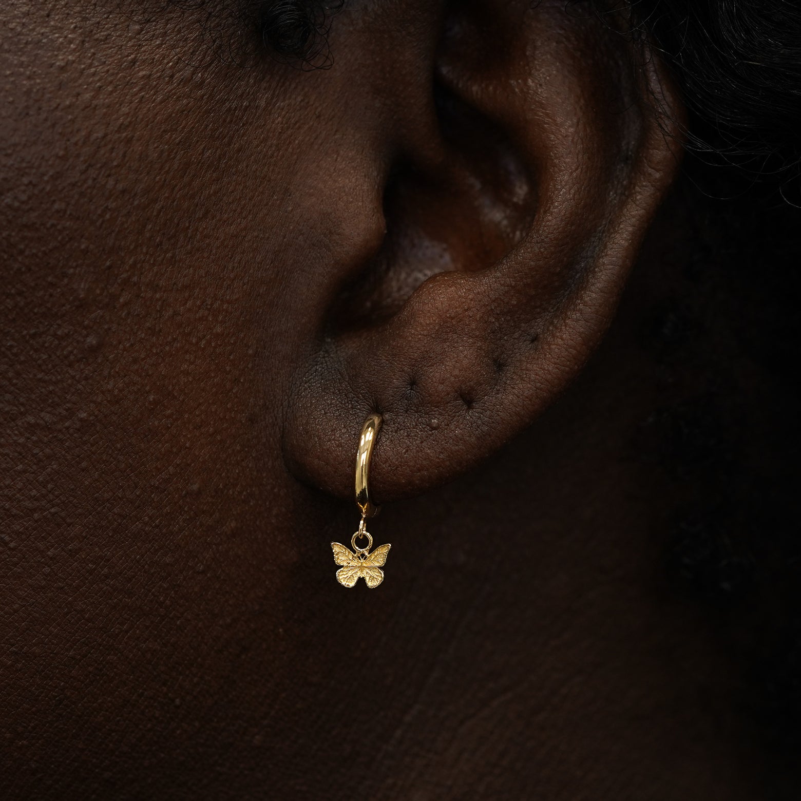 A model wearing a solid 14k gold mini butterfly charm hoop earring