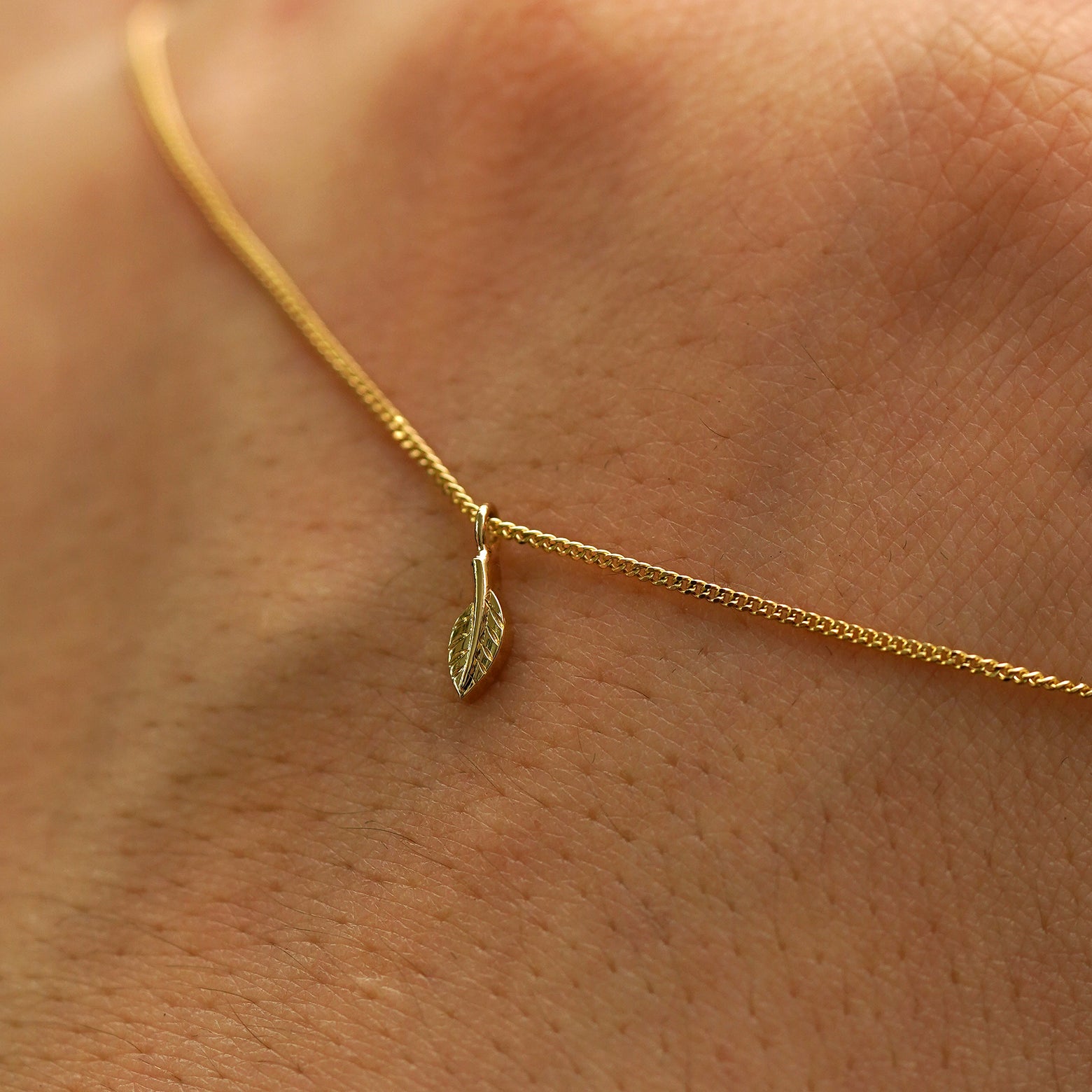 A solid gold mini leaf necklace draped across the back of a model's hand