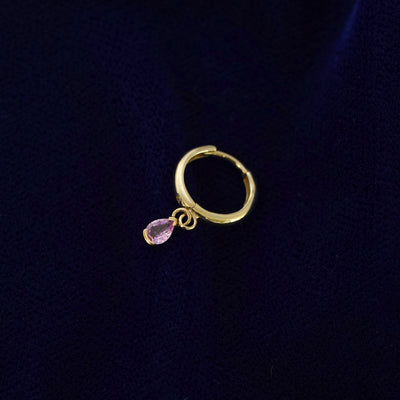 A recycled solid 14k gold Pink Sapphire Dangle Huggie Hoop earring on a dark blue background
