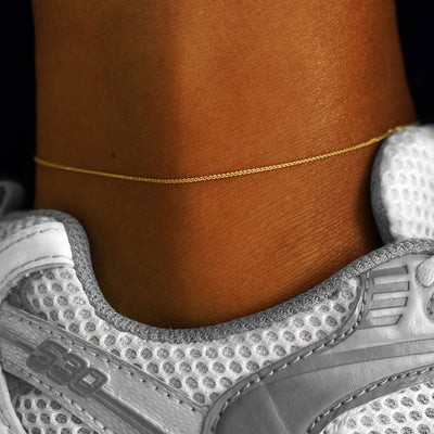 A model's ankle wearing a solid 14k yellow gold Wheat Chain