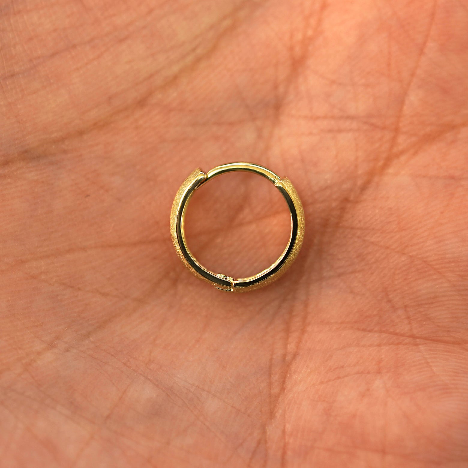 A solid 14k yellow gold Stardust Small Thick Huggie Hoop Earring closed in a model's palm