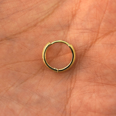 A solid 14k yellow gold Stardust Small Thick Huggie Hoop Earring closed in a model's palm