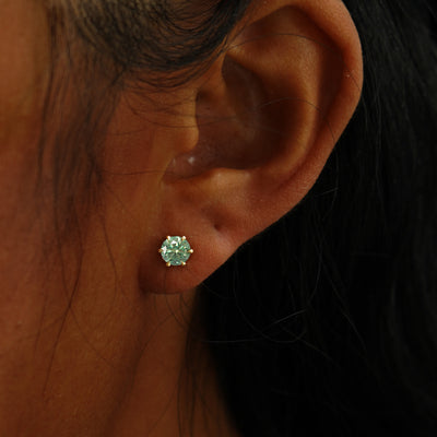 A model's ear wearing a 14k yellow gold green 5mm Moissanite Earring