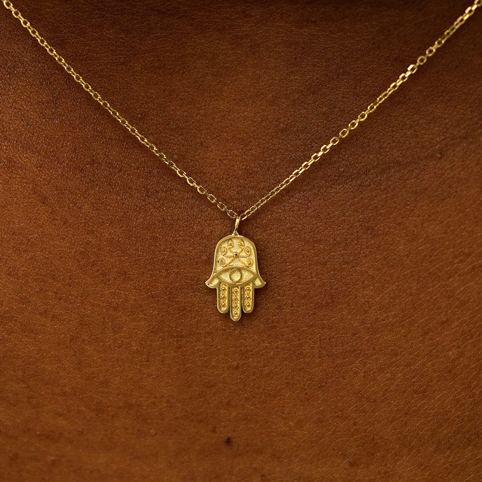 Close up view of a model's neck wearing a 14 karat gold hamsa necklace