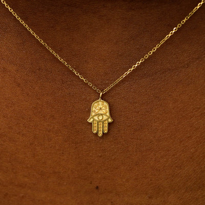 Close up view of a model's neck wearing a 14 karat gold hamsa necklace