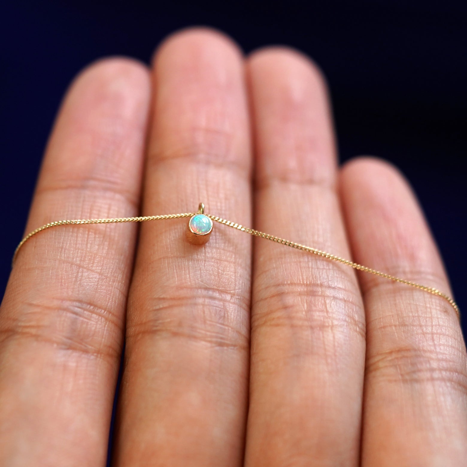 A 14k gold Opal Necklace draped over a model's fingers
