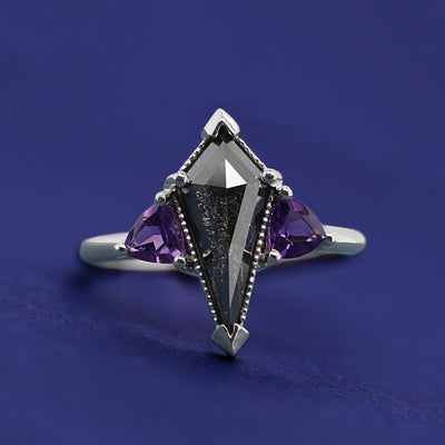white gold ring with dark kite in the center with the sides of triangle purple gems