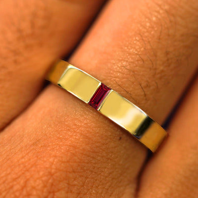 Close up view of a model's hand wearing a solid yellow gold Lab Ruby Baguette Band