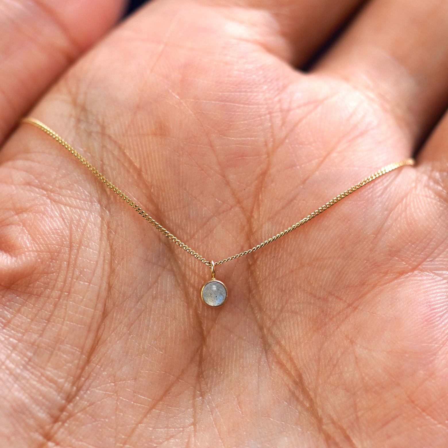 A solid 14k gold Labradorite Necklace resting in a models palm