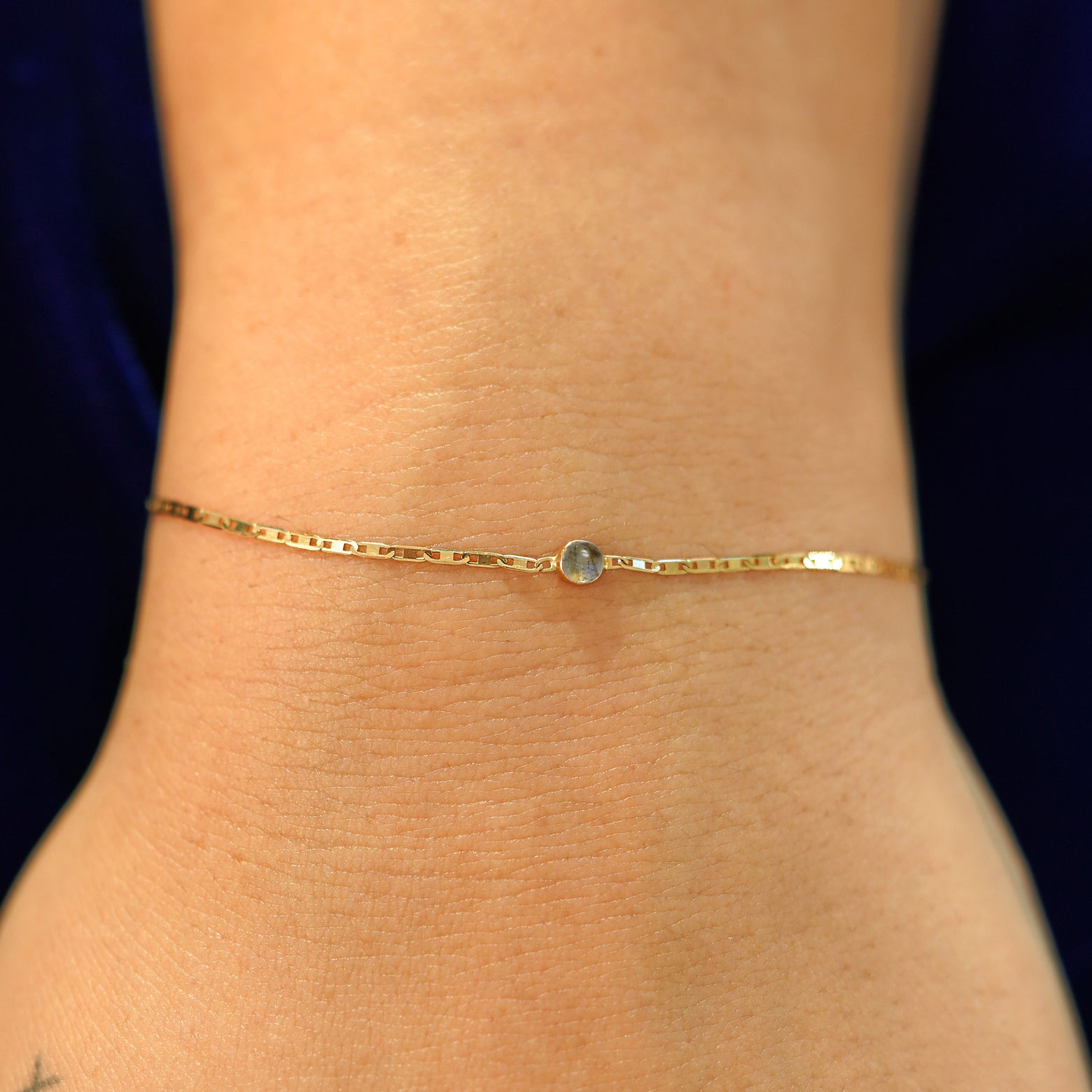 A model's wrist wearing a solid 14k yellow gold Labradorite Bracelet