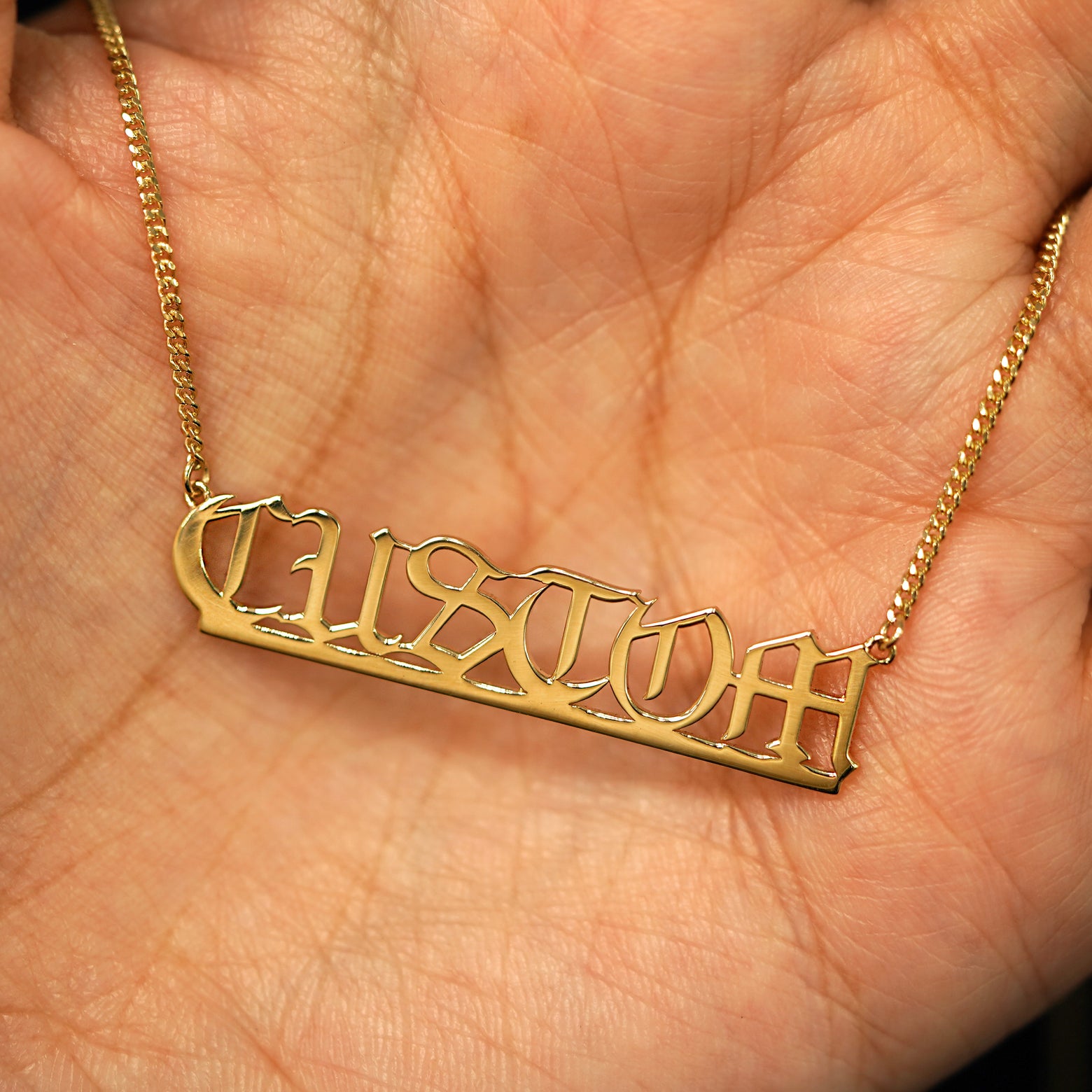 A 14k yellow gold custom nameplate necklace resting in a model's palm