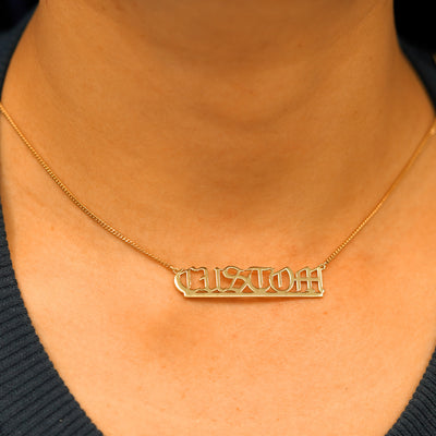 A model's neck wearing a Large Custom Nameplate necklace that reads the word Custom