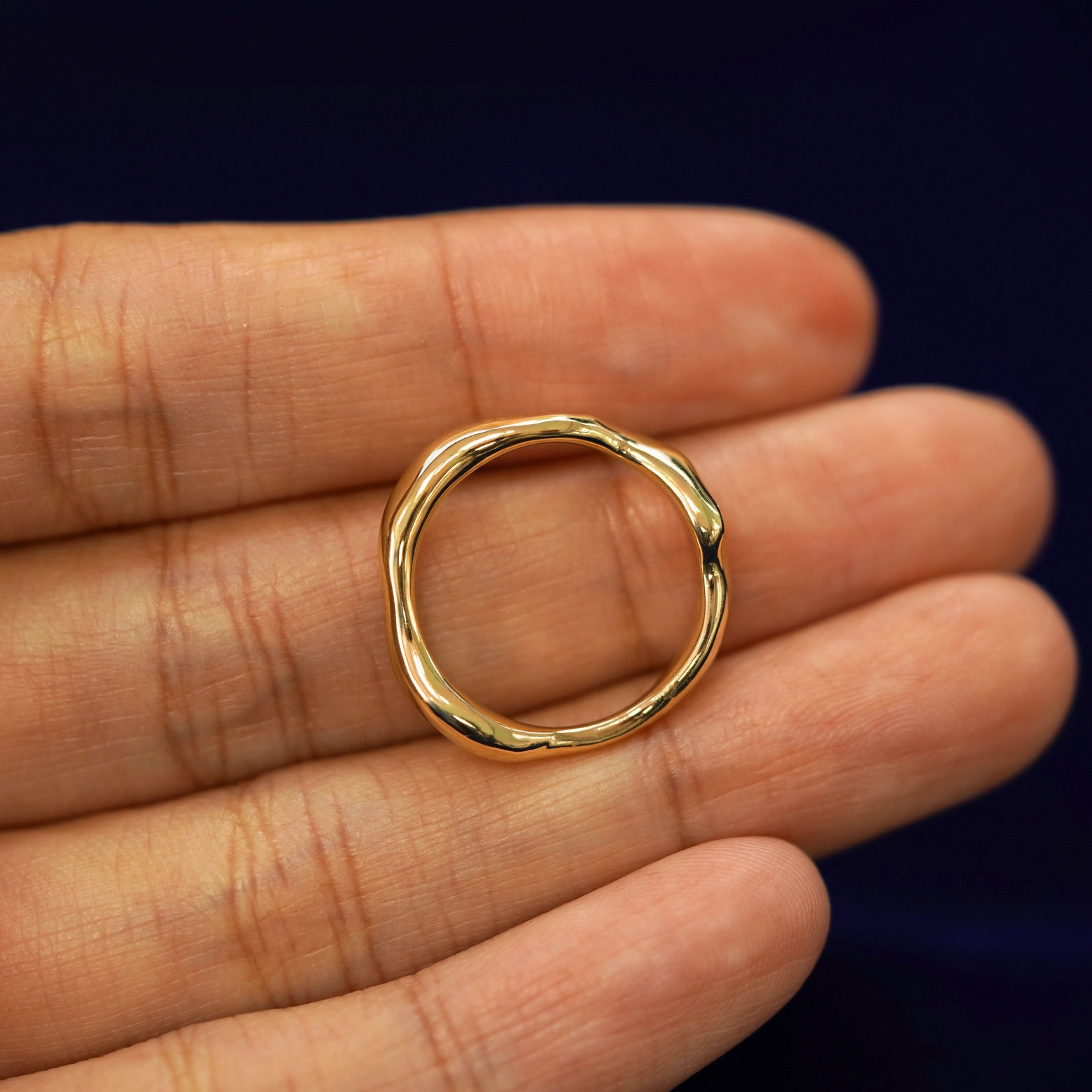 A yellow gold Liquid Band in a model's hand showing the thickness of the band