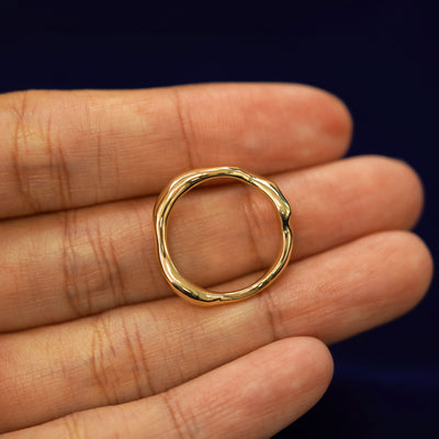 A yellow gold Liquid Band in a model's hand showing the thickness of the band