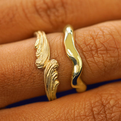 A model's hand wearing a yellow gold Liquid Band and a Crashing Waves Band stacked