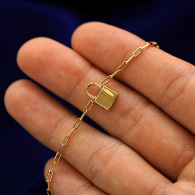 A 14k gold padlock pendant necklace held across a model's fingertips to show details 