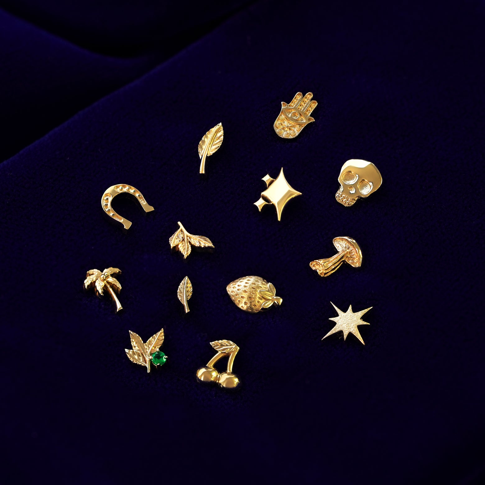 Various 14k yellow gold good luck and nature themed stud earrings on a dark blue cloth background