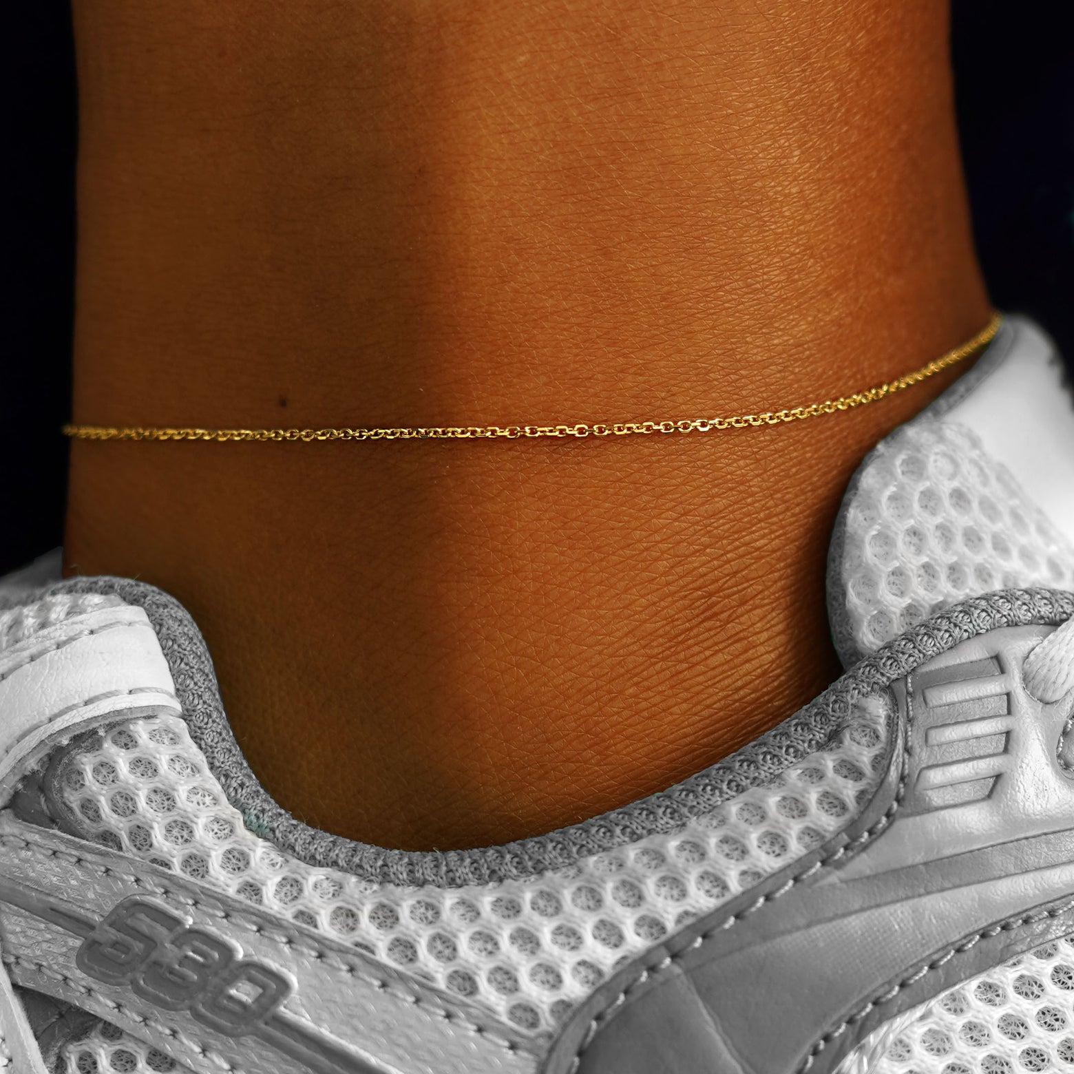 A model's ankle wearing a solid 14k yellow gold Medium Cable Chain