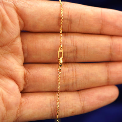 A model's hand holding a yellow 14k gold Medium Cable Chain with an Automic Gold AU lobster claw lock