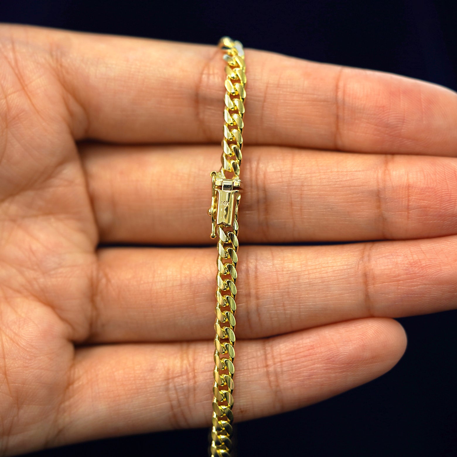 A model's hand holding a yellow 14k gold Medium Miami Chain with a box clasp