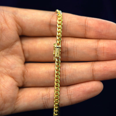 A model's hand holding a yellow 14k gold Medium Miami Bracelet with a box clasp