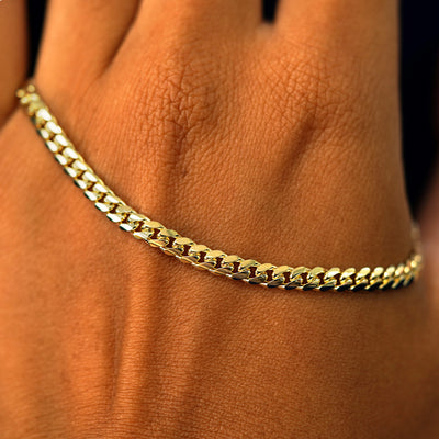 A solid gold Medium Miami Bracelet resting on the back of a model's hand