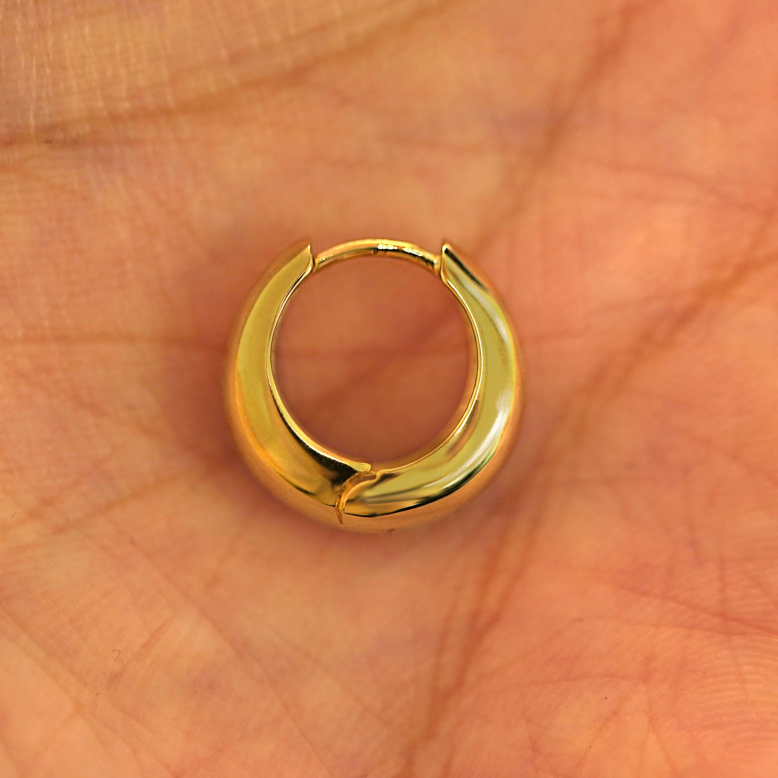 A single closed 14k yellow gold Medium Teardrop Huggie Hoop resting in a model's palm