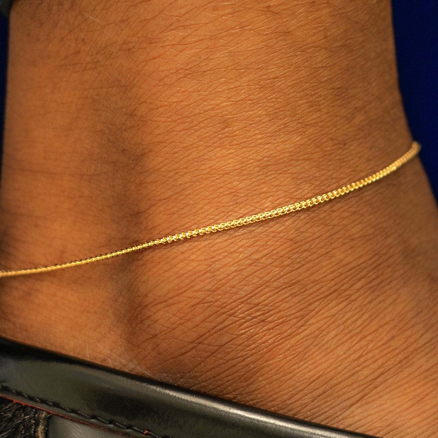 Close up view of a models ankle wearing a solid 14k yellow gold Mini Franco Chain Anklet