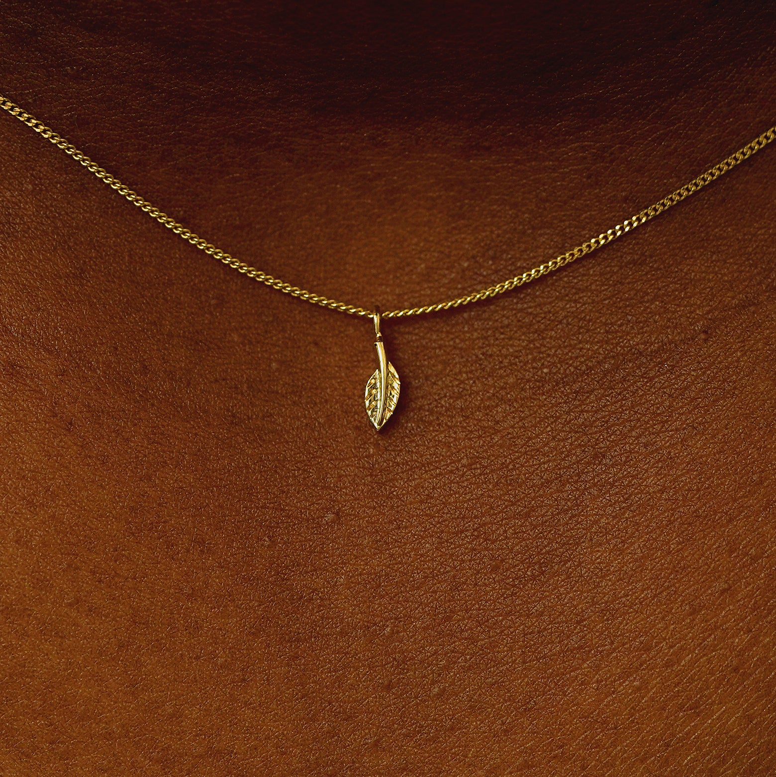 Close up view of a model's neck wearing a 14 karat gold mini leaf necklace