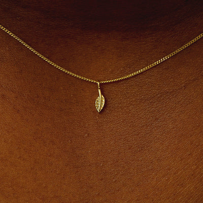 Close up view of a model's neck wearing a 14 karat gold mini leaf necklace